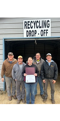 Five Vernon County workers pose with their award outside in front of a recycling drop off building.