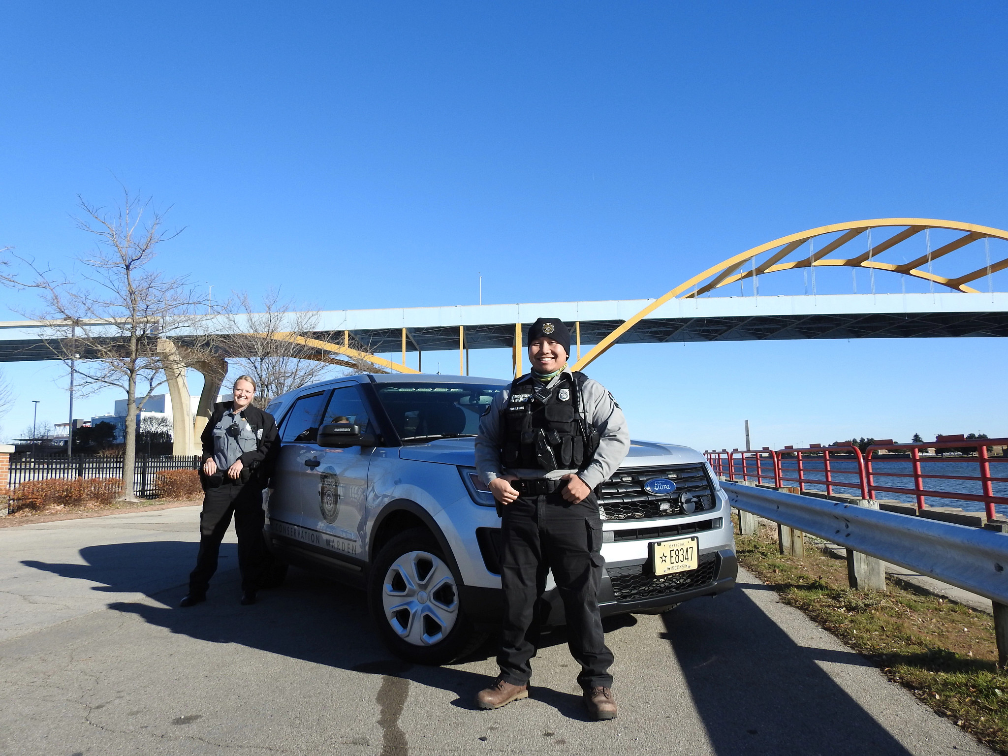 two DNR conservation wardens standing in front of a DNR vehicle on a bridge
