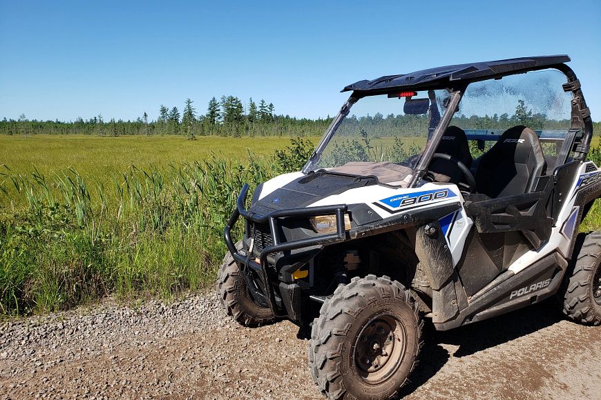 A UTV parked on a gravel trail next to a green field.