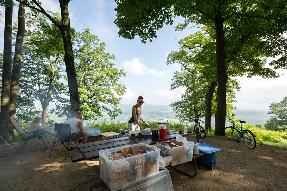Three people sit around a campfire next to a picnic table while admiring the views from an elevated campsite at Wyalusing State Park