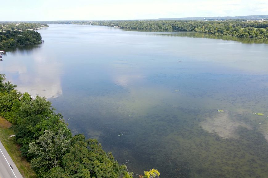 An aerial view of a large lake stretching over the horizon, giving way to tree cover.