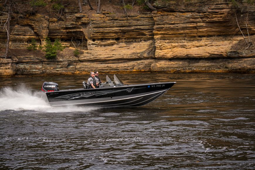 two uniformed male conservation wardens on a boat with rock structure in the background