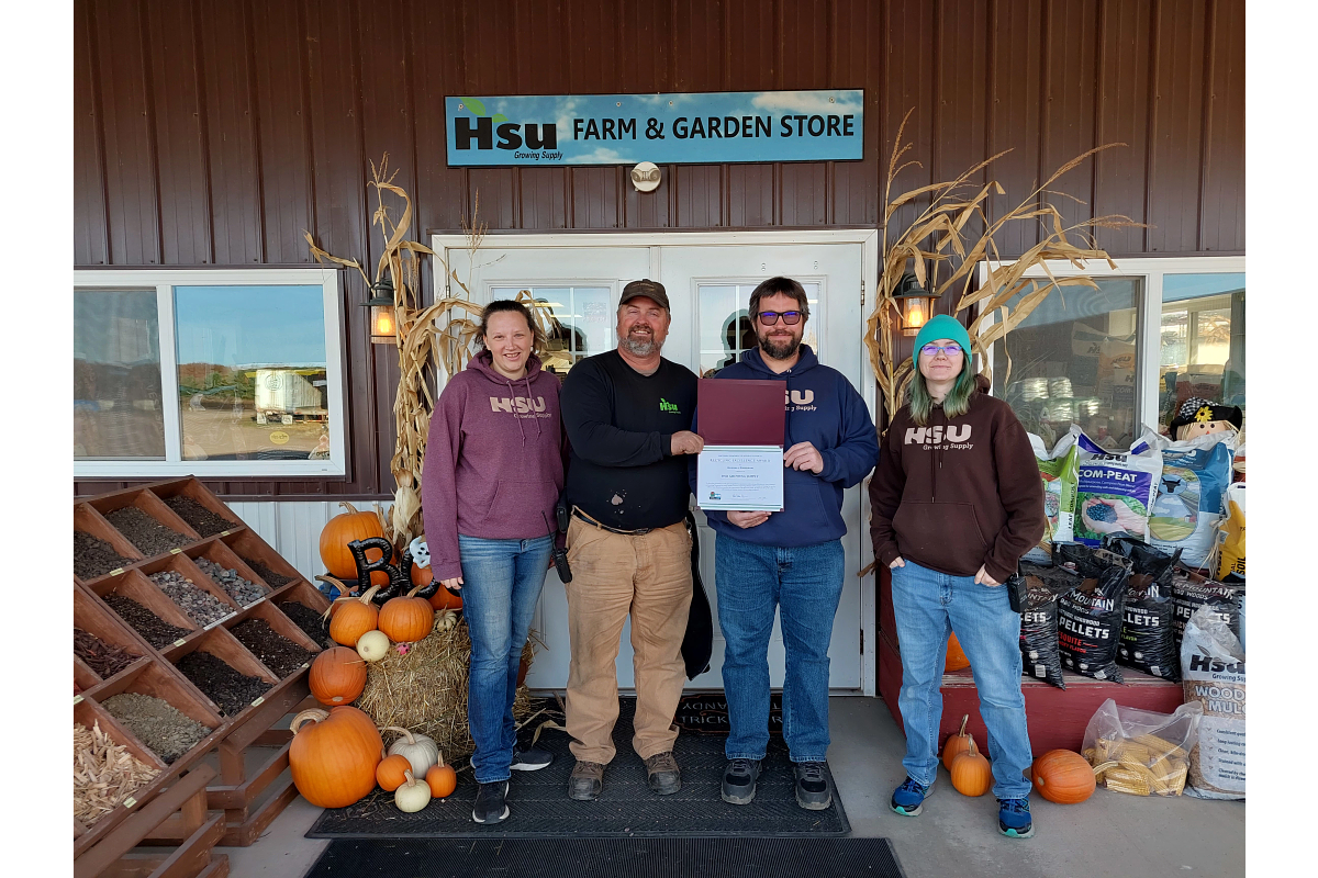 Four Hsu representatives stand in front of their building with their award. Around them are pumpkins and bins of compost.