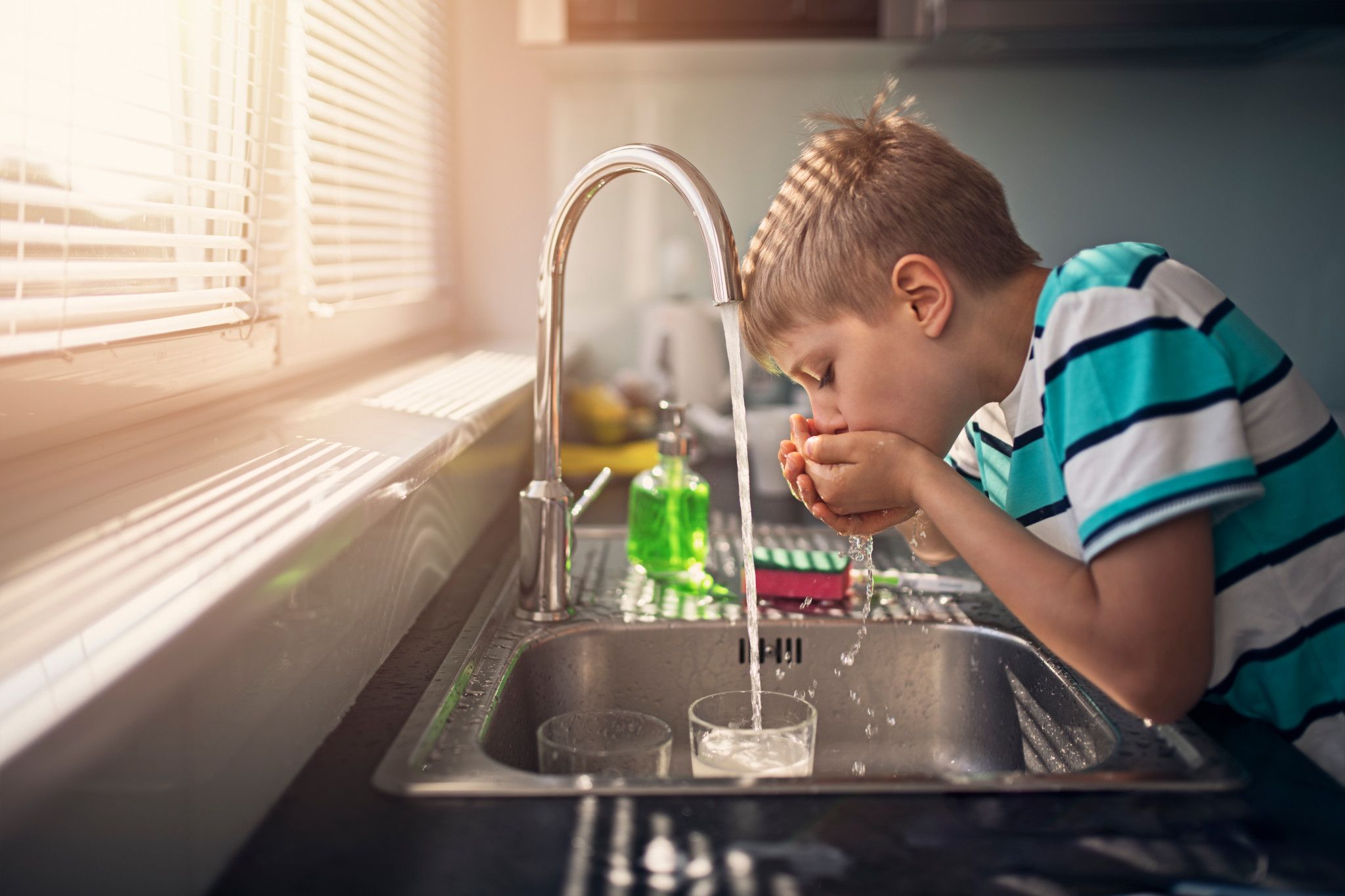An image of a boy drinking water from the sink. 