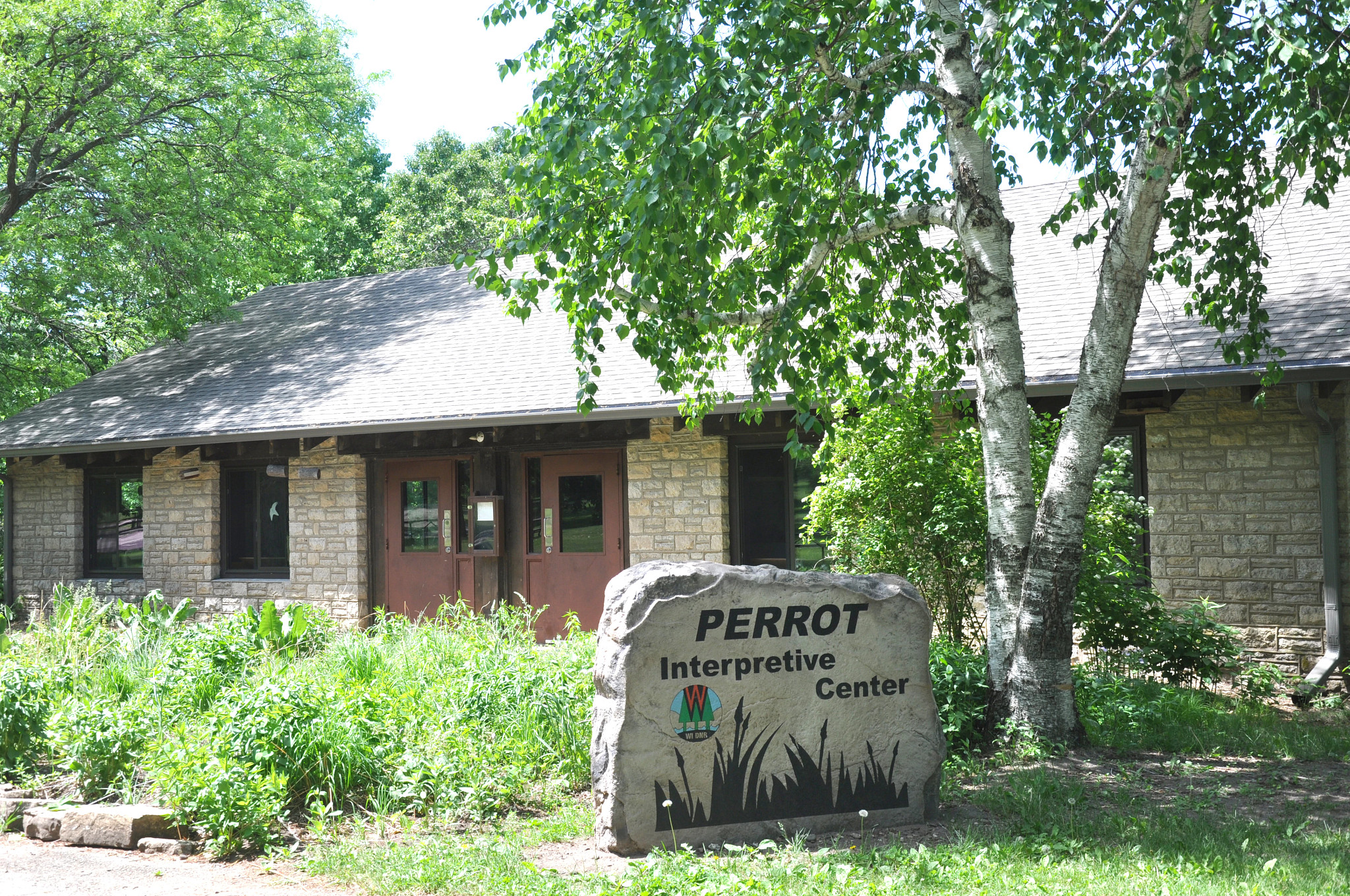Exterior image of the interpretive center at Perrot with a stone sign and green foliage.