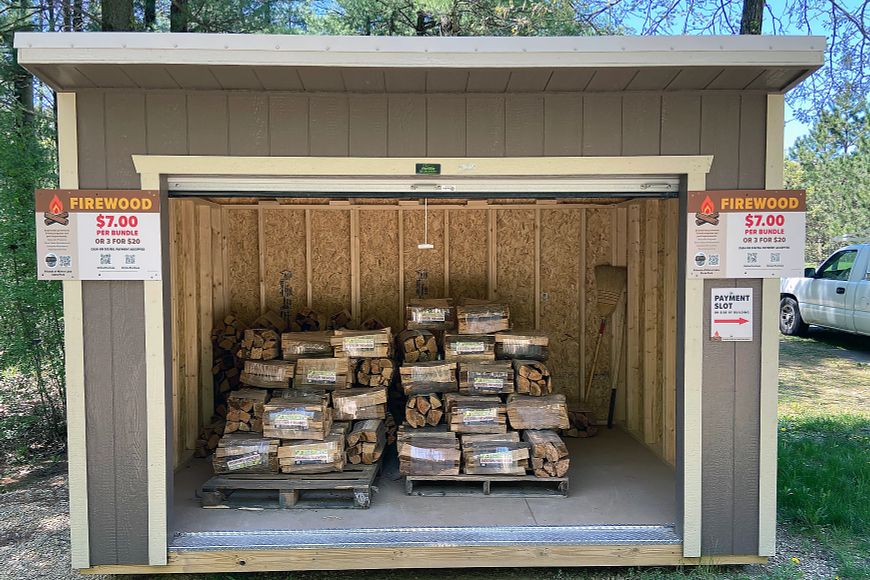 A brown shed filled with cut firewood stacked on pallets.