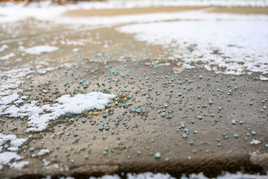 A close, focused low angle view of salt, ice and snow on a patch of concrete.
