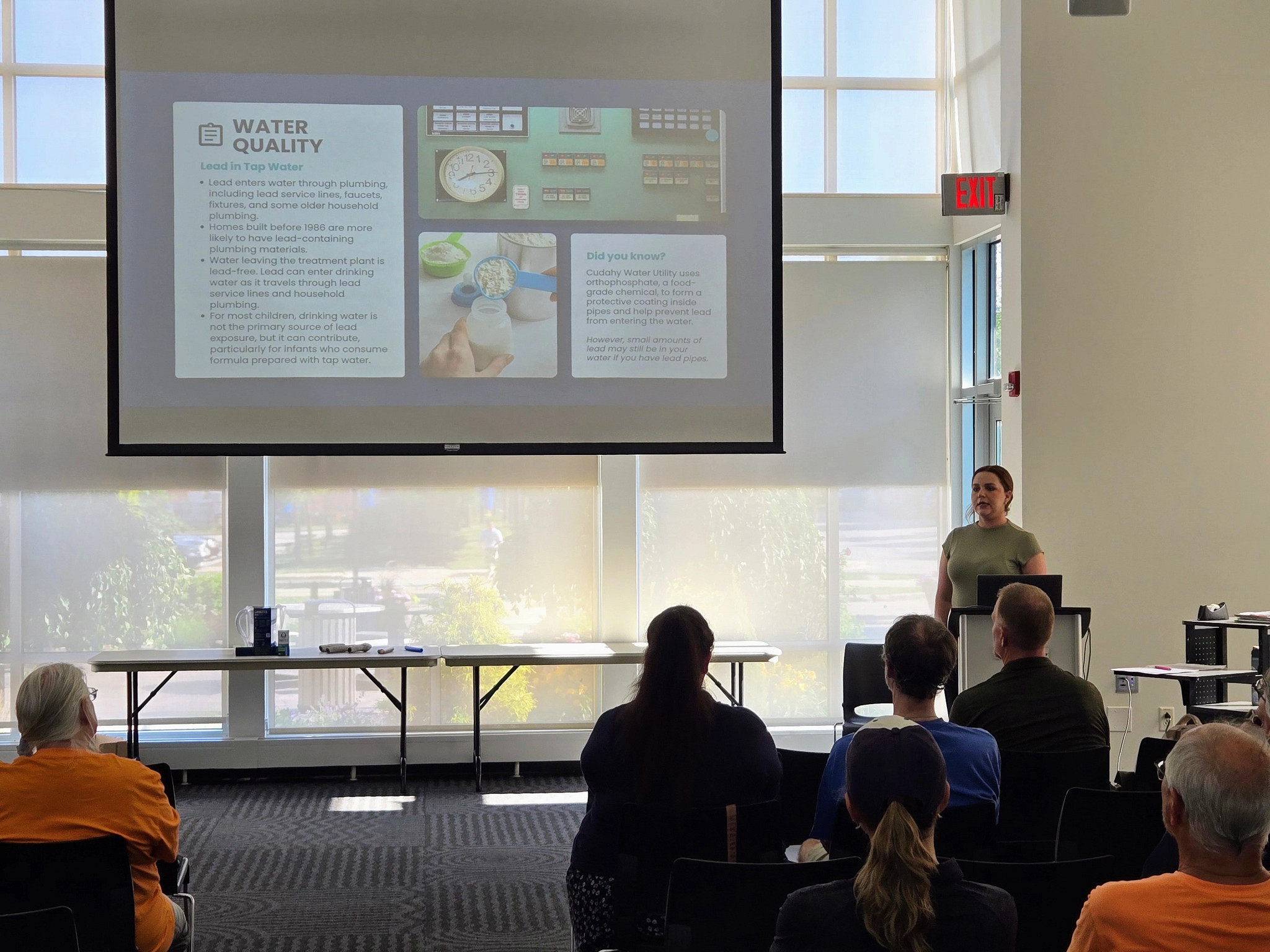 a woman giving a presentation to people at an informational meeting about water quality and lead.
