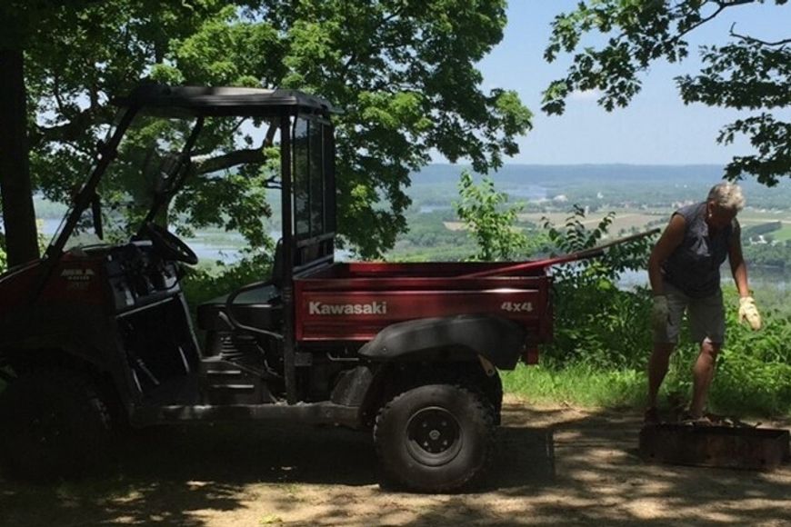 A male campground host cleaning up a campsite at a state park with a red ATV in the background