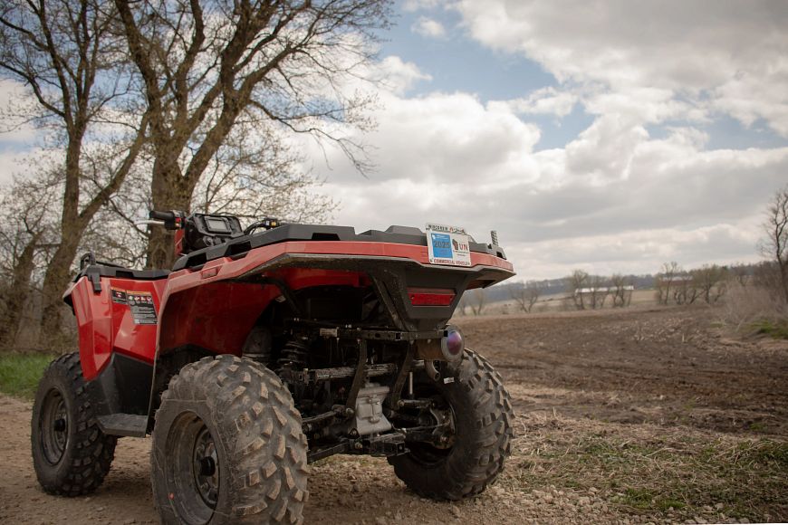 A red ATV is parked on a gravel trail next to a tilled field. 