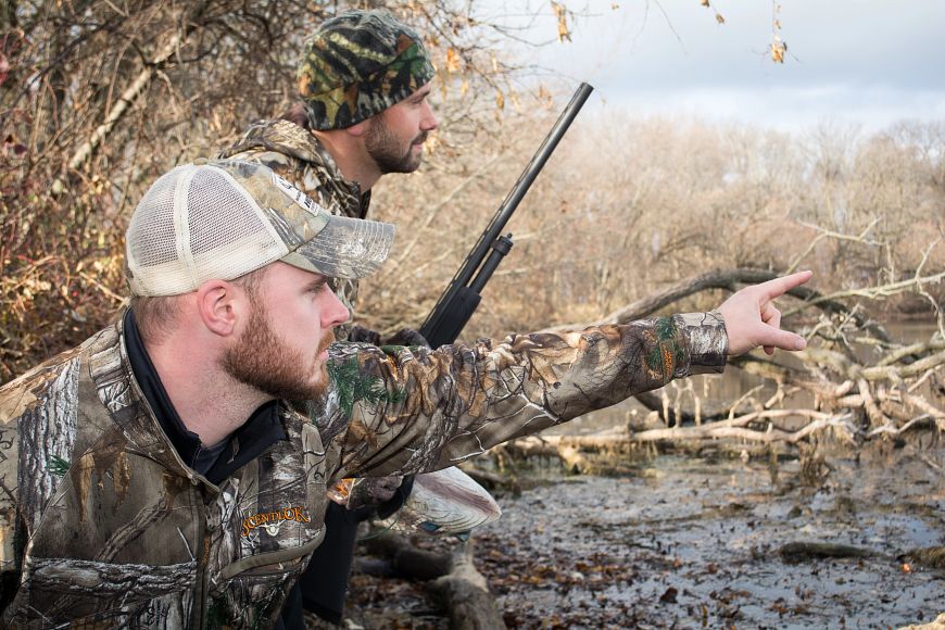 two men wearing camouflage hunting near wetlands
