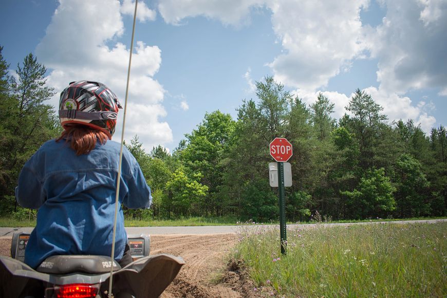 a woman wearing a helmet riding an ATV and stopping at a stop sign