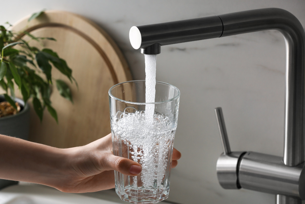 A person fills up a glass with water from a kitchen sink.