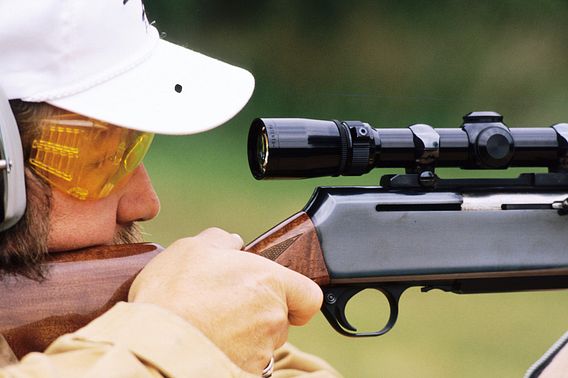 A shooter looking through the scope of a gun while wearing eye and ear protection