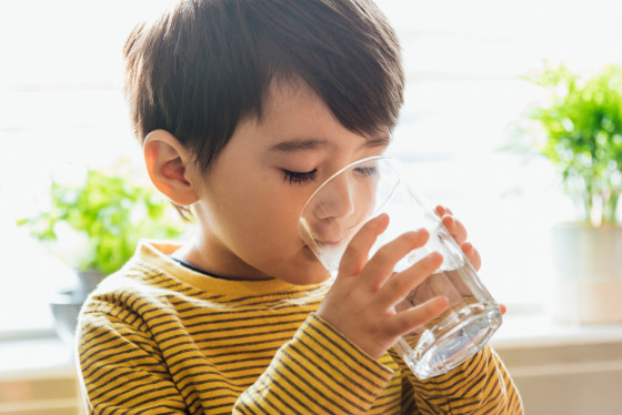 A young boy drinks a glass of water.