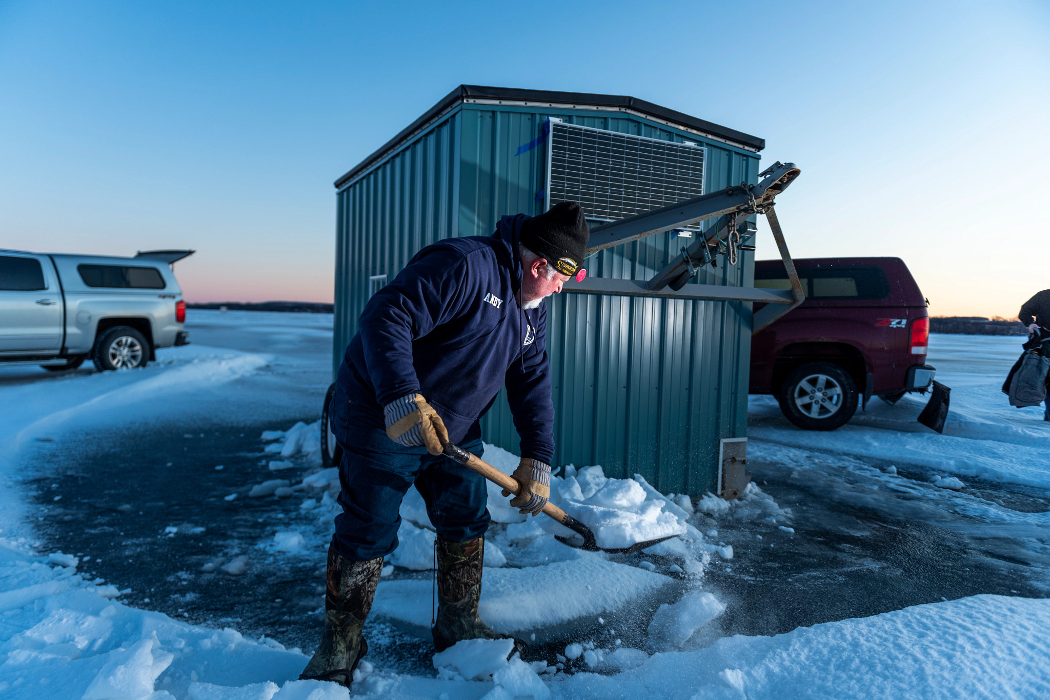 man shoveling snow around his sturgeon spearing shack on ice-covered lake