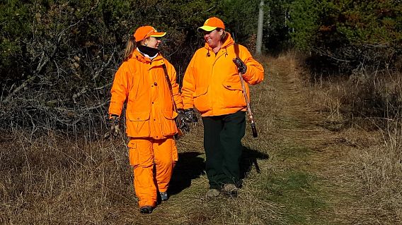 two orange-clad women hunters walking in the woods