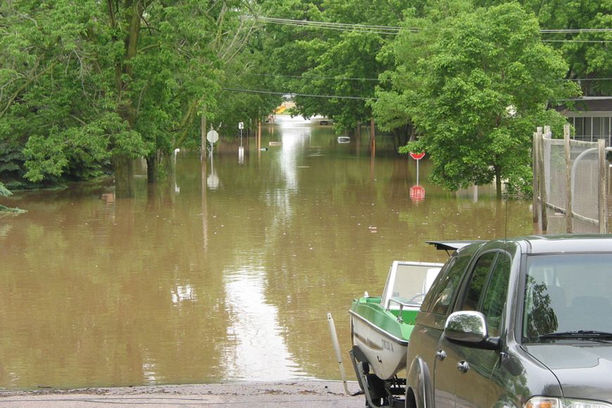 a truck pulling a boat on a trailer near floodwaters in a flooded city.
