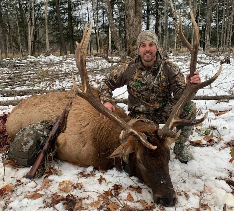 An image of a hunter standing in front of his harvested elk.