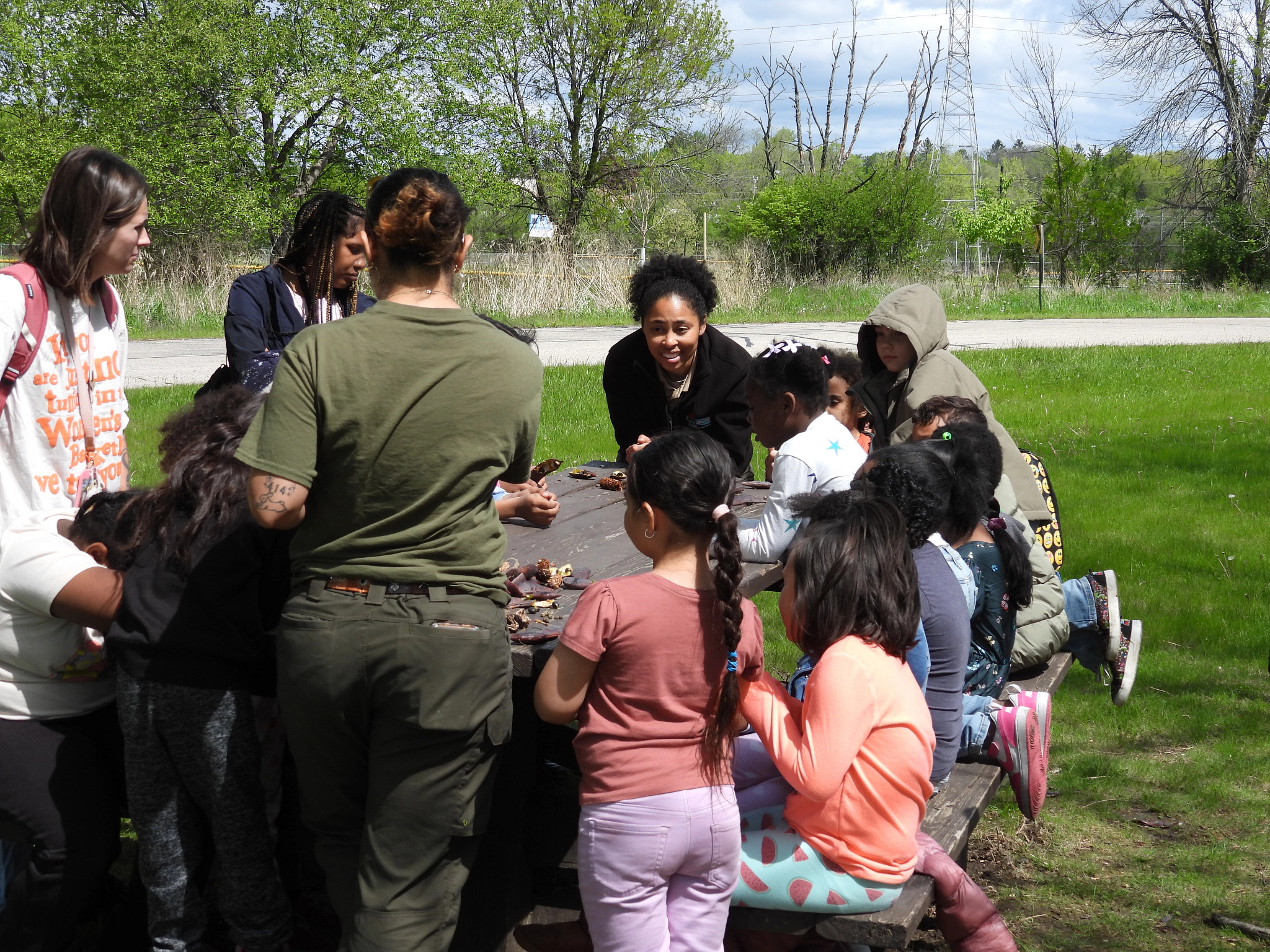 Class of kids looks at small natural items like pinecones with a DNR Staff member and parents.