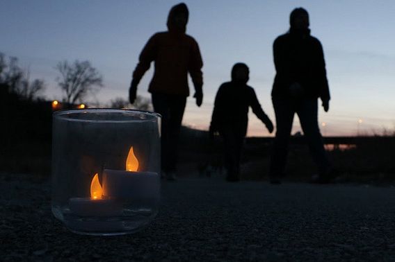 The silhouette of a family walking along a candlelit trail.