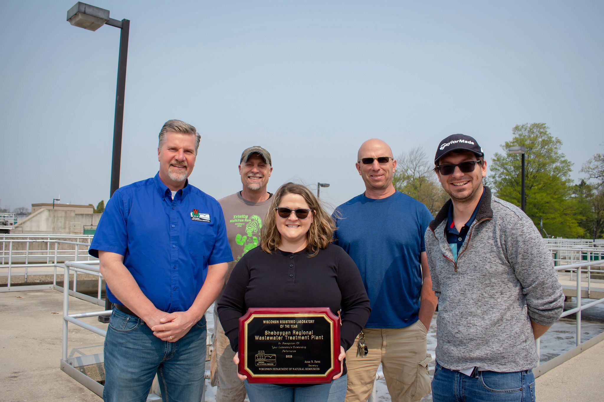 Sec. Adam Payne beside the lab's team on the roof of the wastewater treatment lab on a sunny day