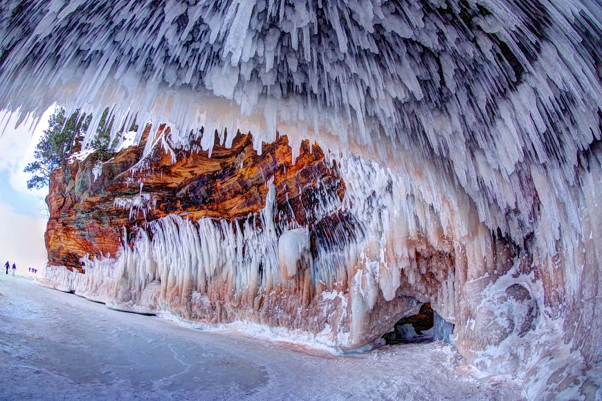 Icicles and ice formations adorn a coastal cave alongside a frozen lake. 