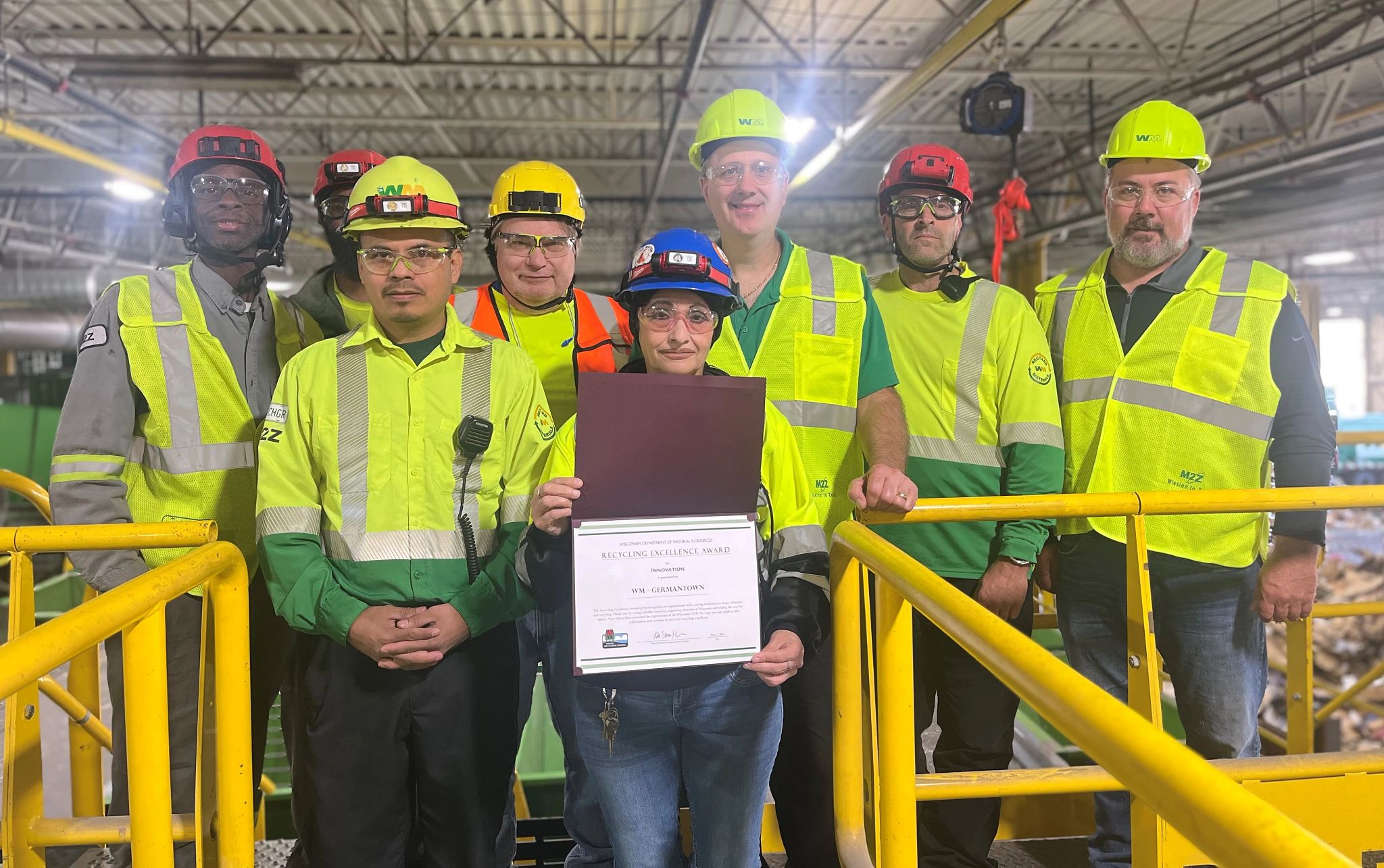 Eight WM-Germantown workers pose in their facility with their award. All eight wear hard hats and bright yellow protective vests.