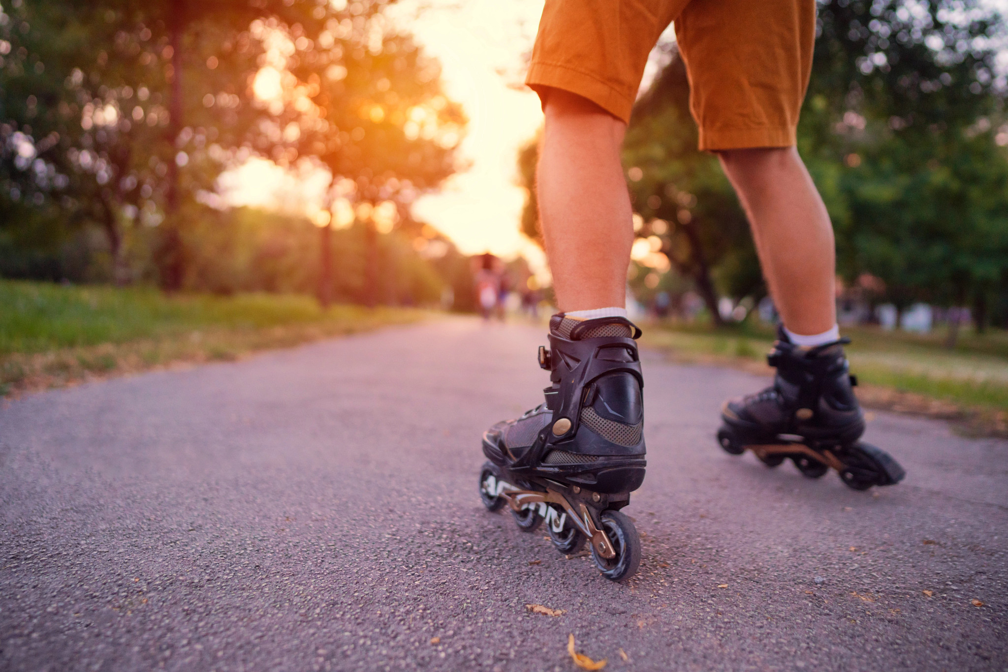 unidentifiable man rollerblades on a trail with a setting sun behind him, cropped legs down.