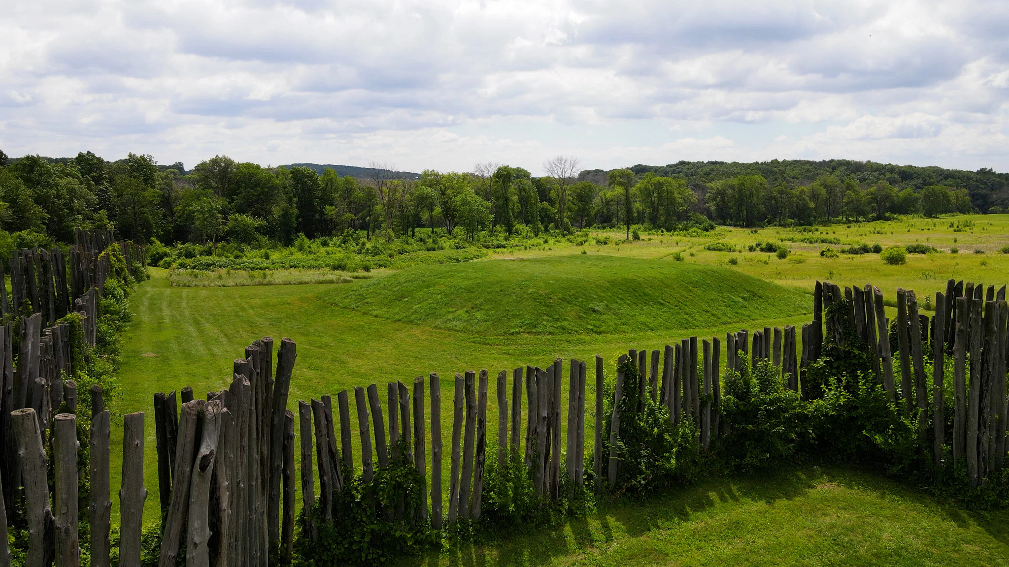 Aerial image of a wooden post fence and ancient building foundations now covered in green grass.