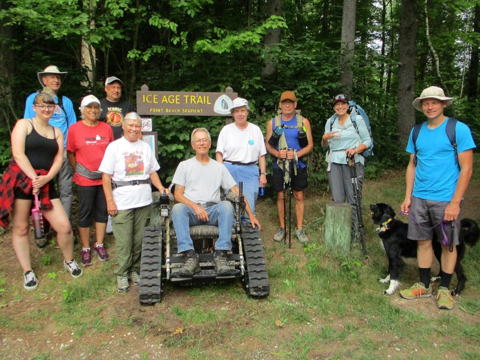 group of people pose next to man in adaptive wheelchair in front of ice age trail sign