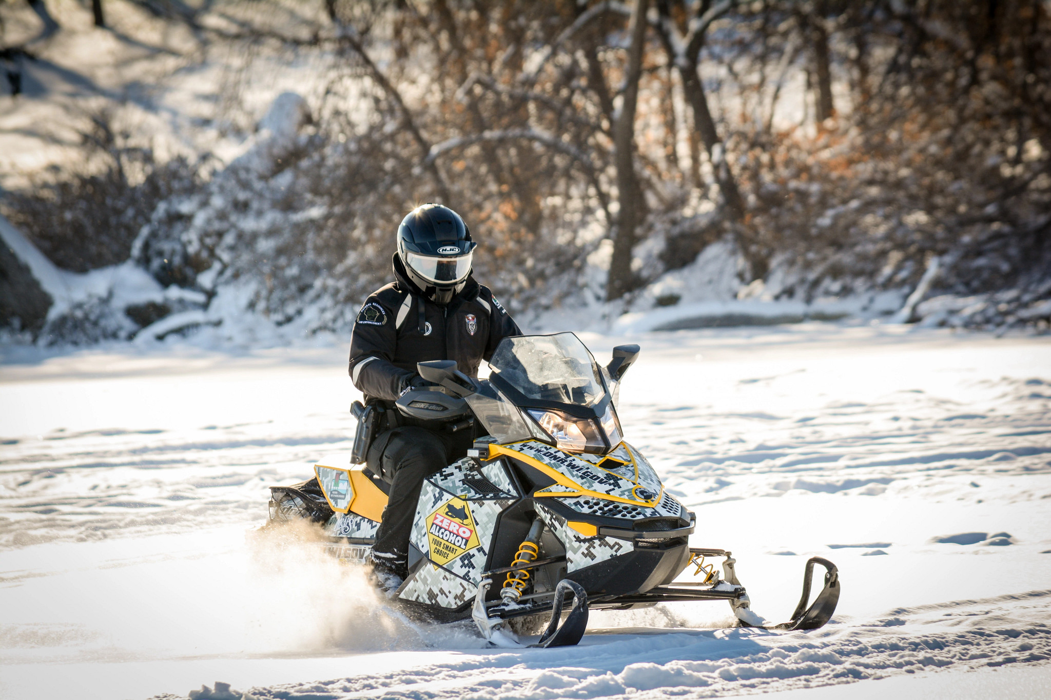 Wisconsin DNR conservation warden riding a snowmobile with a decal that says "Zero alcohol" on a frozen lake