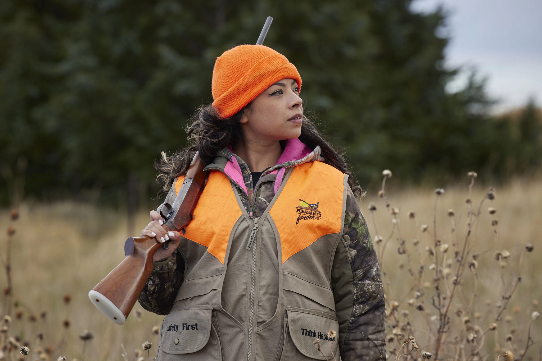 female hunter wearing blaze orange standing in field holding gun