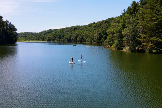 An aerial view of two people stand-up paddleboarding on a calm lake beneath a brilliant blue sky.