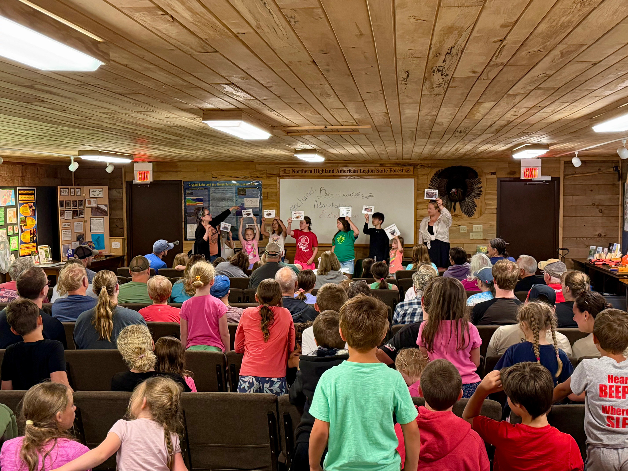 Children stand and listen as other kids give a presentation in the nature center.