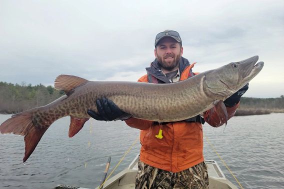 A man in an orange float coat holds a large musky.