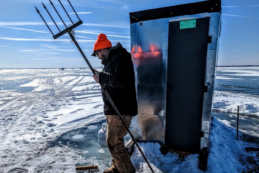 a man holding a sturgeon spear on ice near shanty