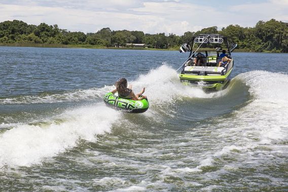 A woman in a green innertube is pulled behind a boat on a lake.