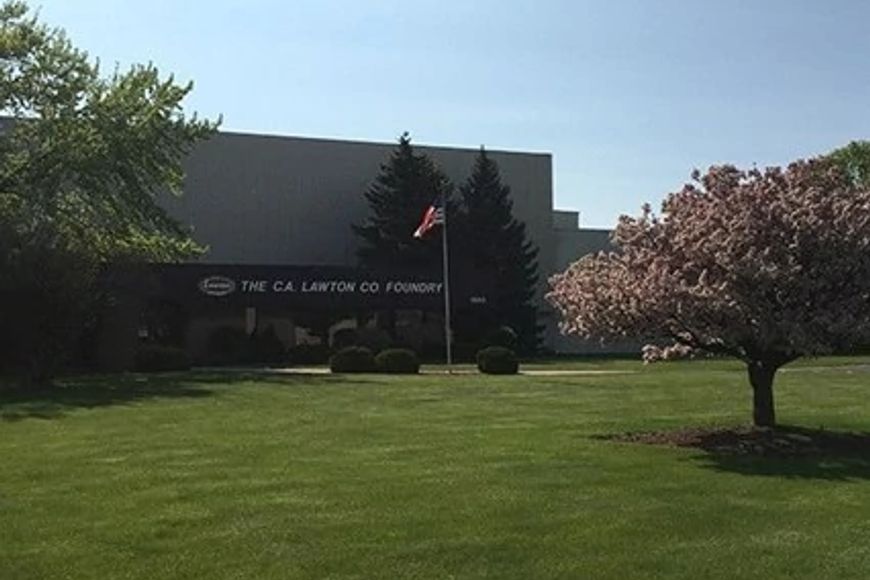 A large building with an American flag and manicured lawn has the words "The C.A. Lawton Co. Foundry" on its brick exterior.