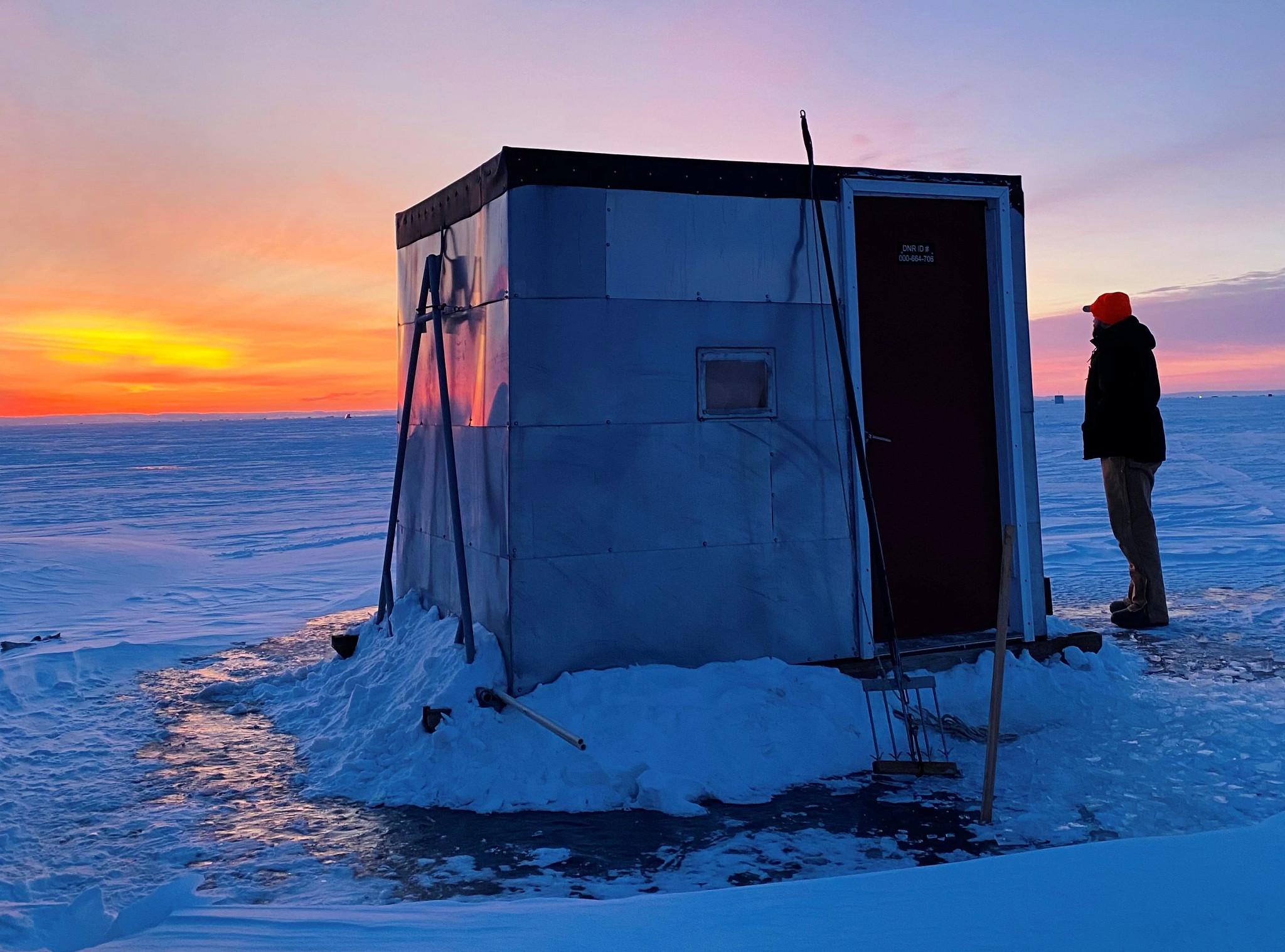 someone standing near fishing shanty on ice at sunrise with sturgeon harvesting tools