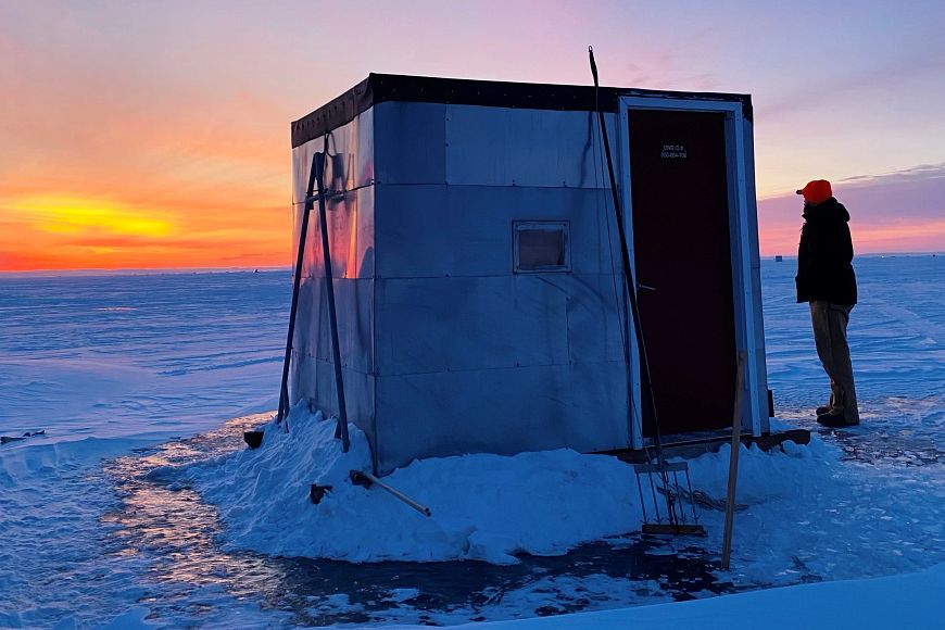 someone standing near fishing shanty on ice at sunrise with sturgeon harvesting tools