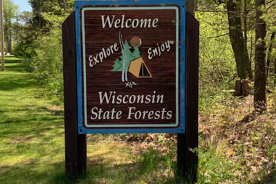A brown wooden sign welcomes visitors to a Wisconsin state forest