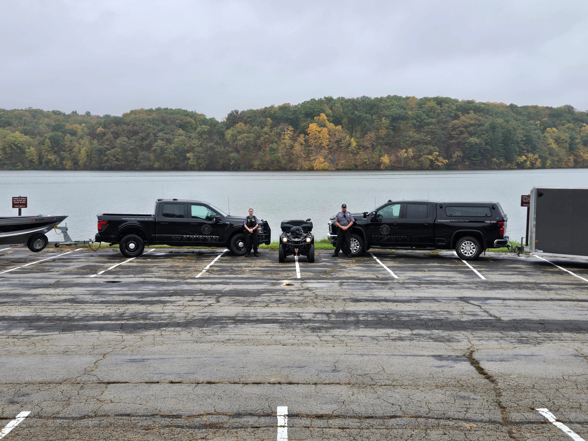 two wardens standing in front of trucks pulling boats and an ATV in front of lake at Yellowstone Lake State Park