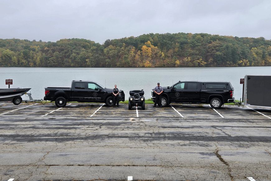 two wardens standing in front of trucks pulling boats and an ATV in front of lake at Yellowstone Lake State Park