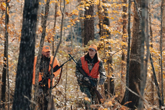 Two hunters wearing blaze orange walk in the woods. 