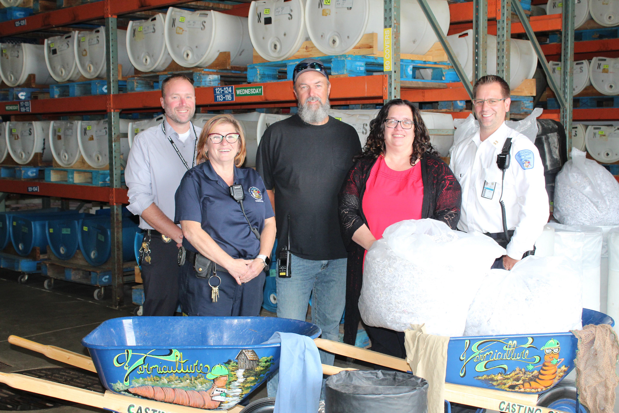 Five people standing in a warehouse setting pose for a group photo. 