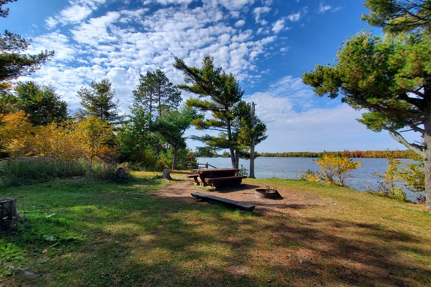 a forested campsite along the water in Turtle Flambeau Scenic Waters Area with a firepit and picnic table
