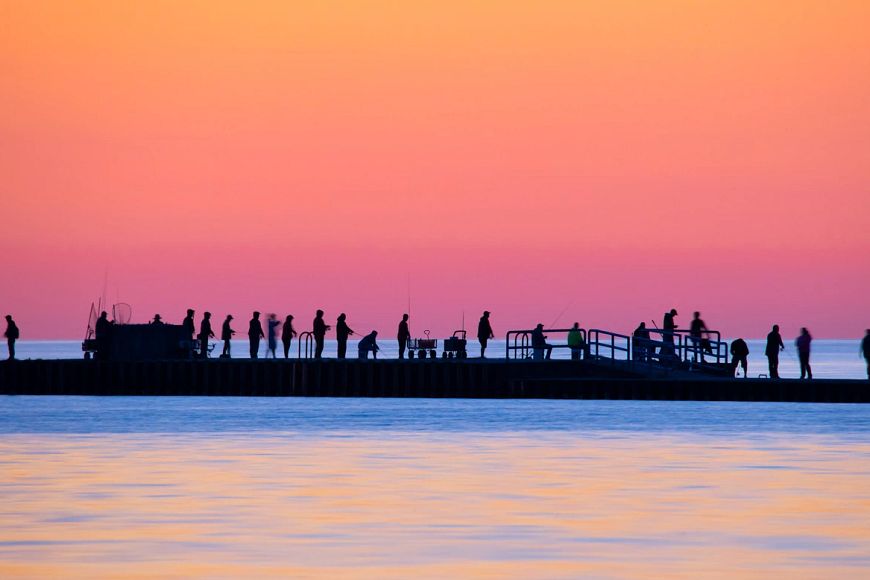 A group of people fishing on a pier in Lake Michigan at sunrise.