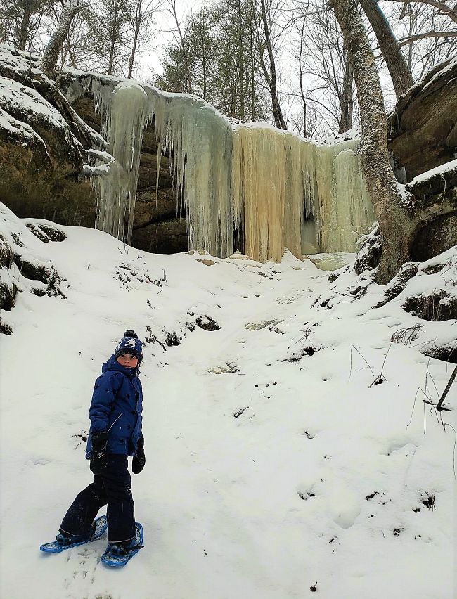 boy snowshoeing by frozen waterfall