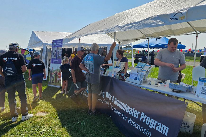 A group of DNR staff talks with community members under a large white tent at a public event.
